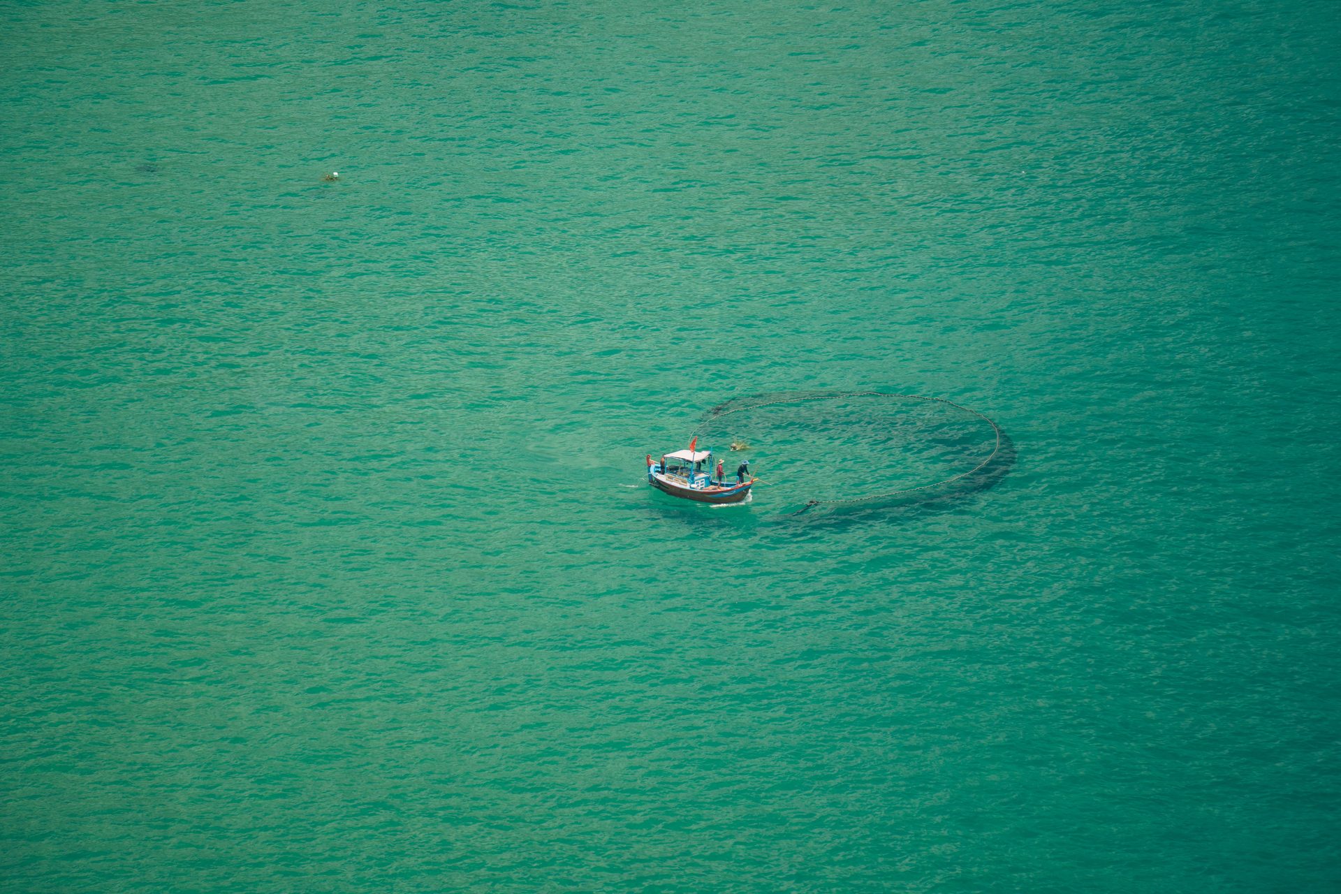 Fishers casting a circular net in the turquoise water near Mũi Điện, photographed from the headland above