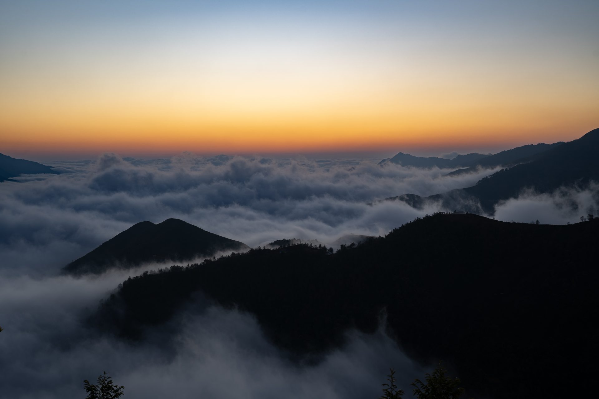 Dawn breaks above a sea of clouds between the dark mountain ridges